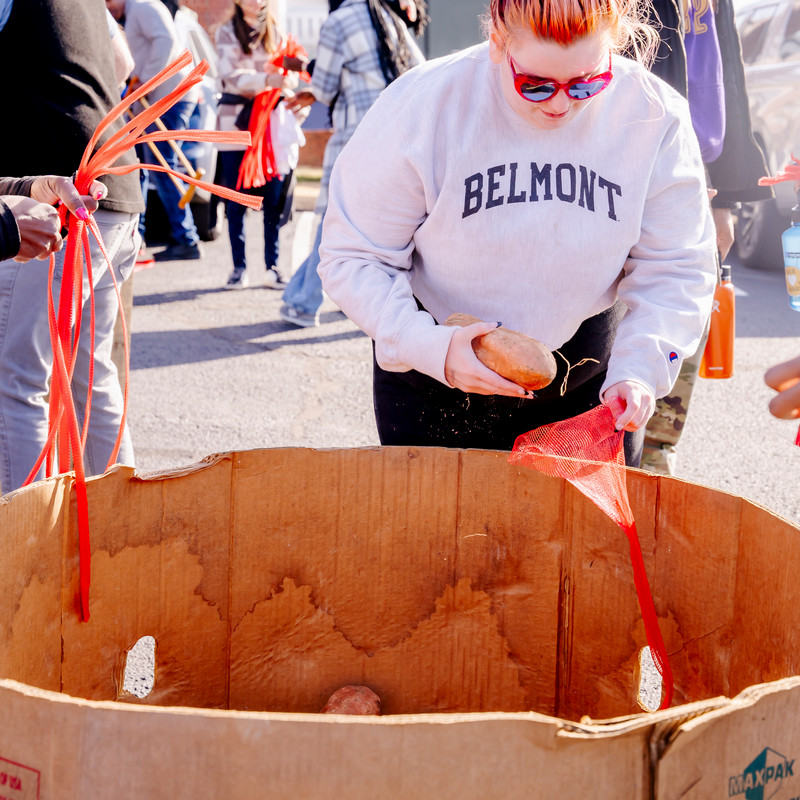 Student in a Belmont sweatshirt lifts sweet potato from box into a bag