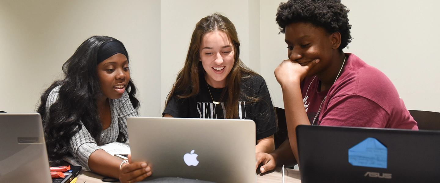 Three Belmont Student looking at their laptops while huddled together