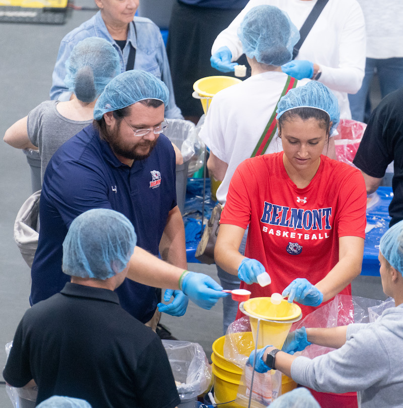 two volunteers pour oatmeal into a bag