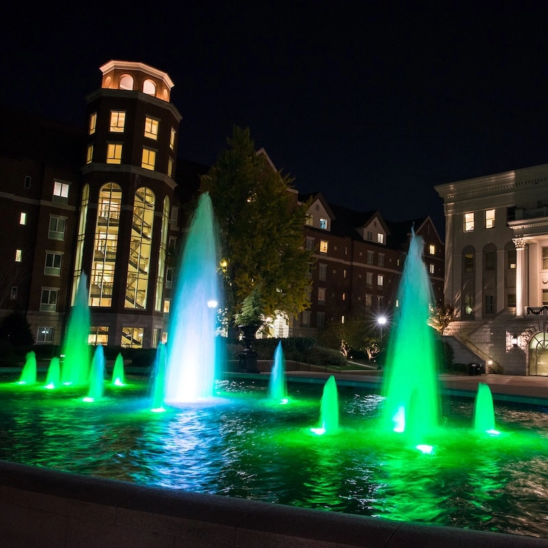 Nighttime view of a vibrant fountain surrounded by buildings, showcasing colorful lights