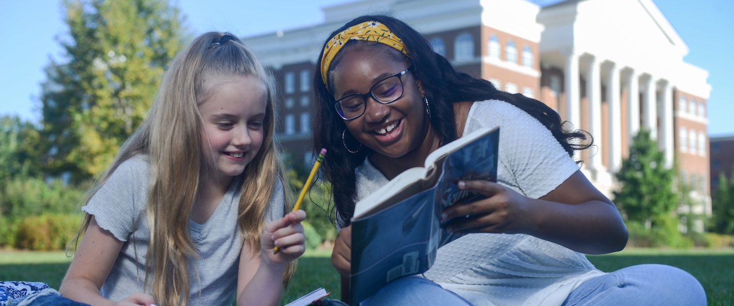 Chasity reads to a student on the lawn