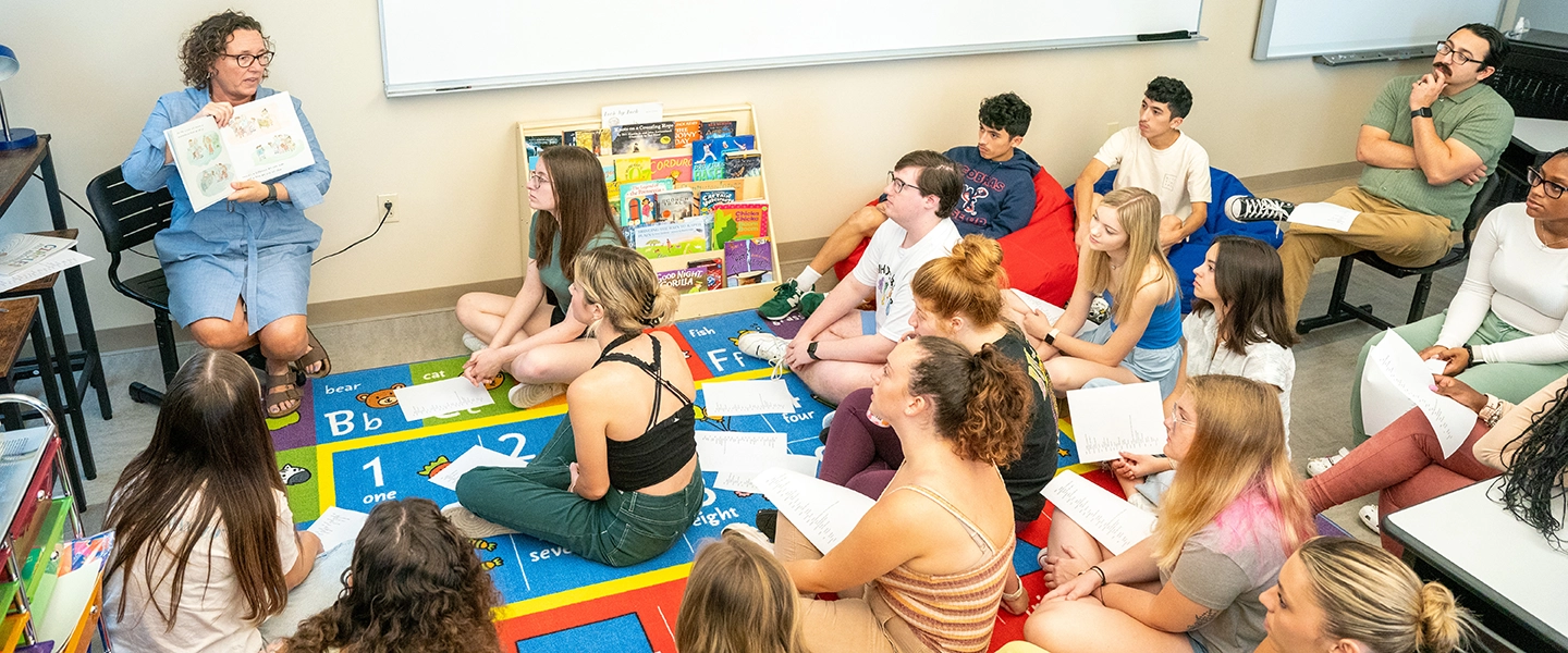 Dr Rachael Flynn reads aloud to a group of education students that are seated on the carpet in front of her