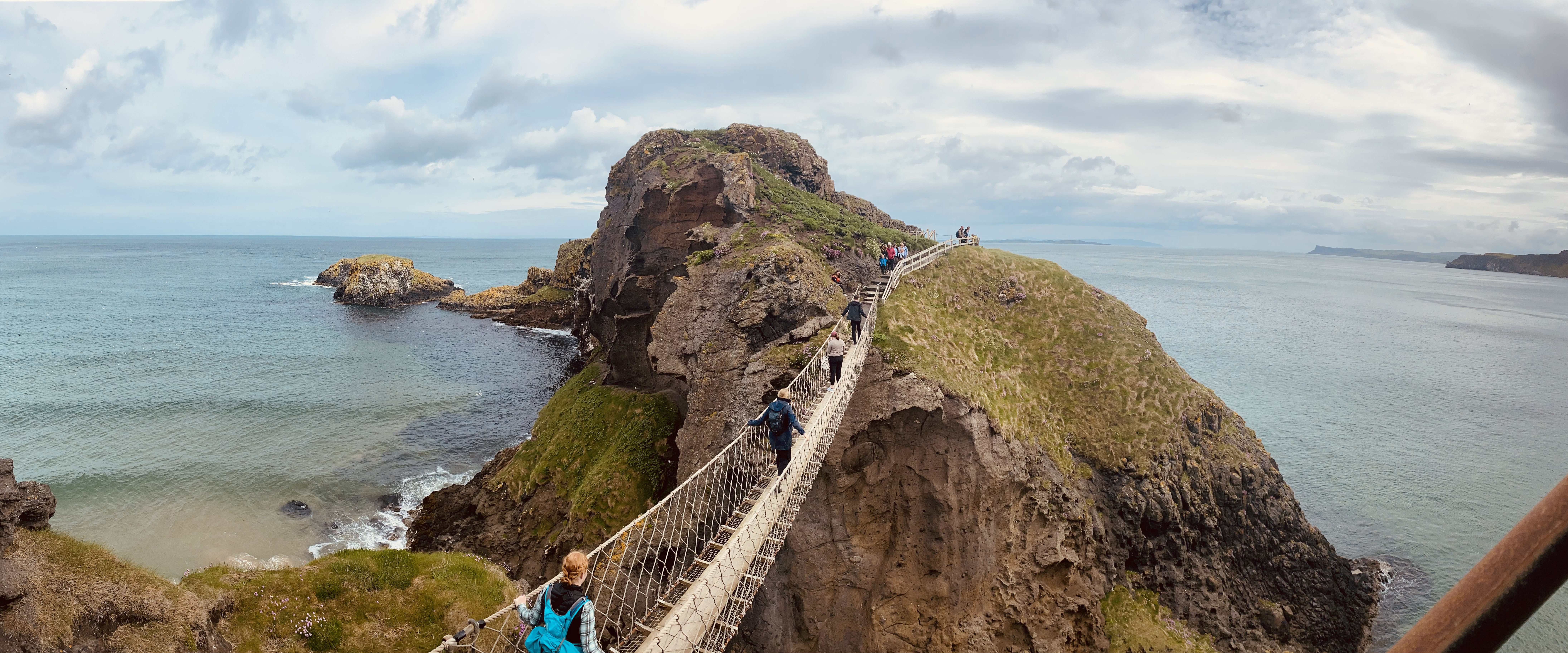 People walking across rope bridge in Ireland cliffside
