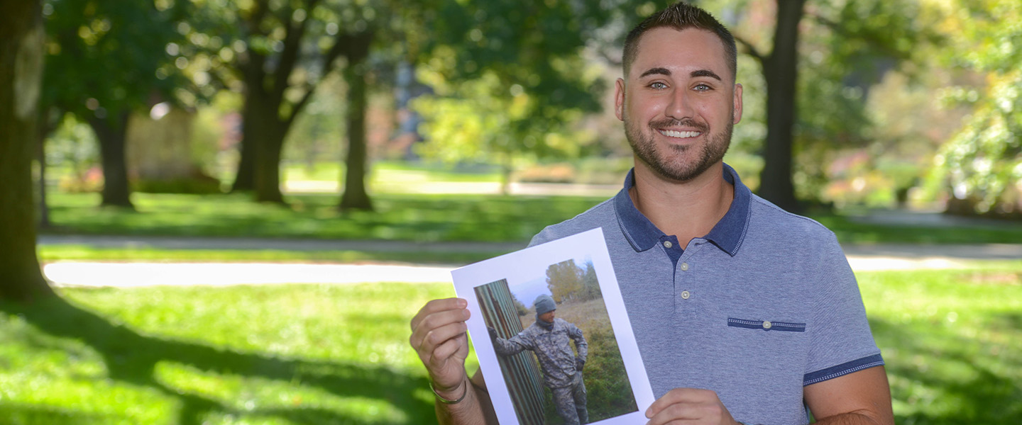 A male veteran holding a photo of himself when he served