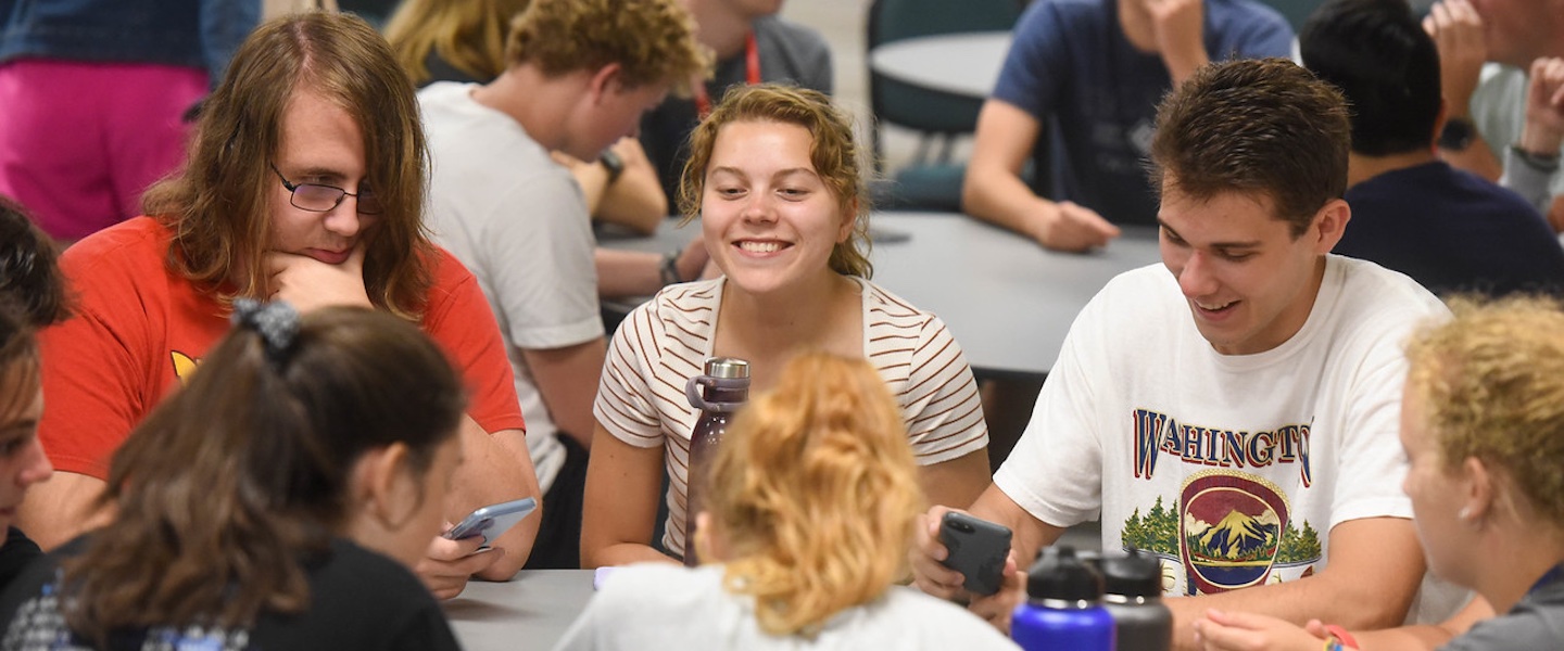 Student smiles at a table with other students