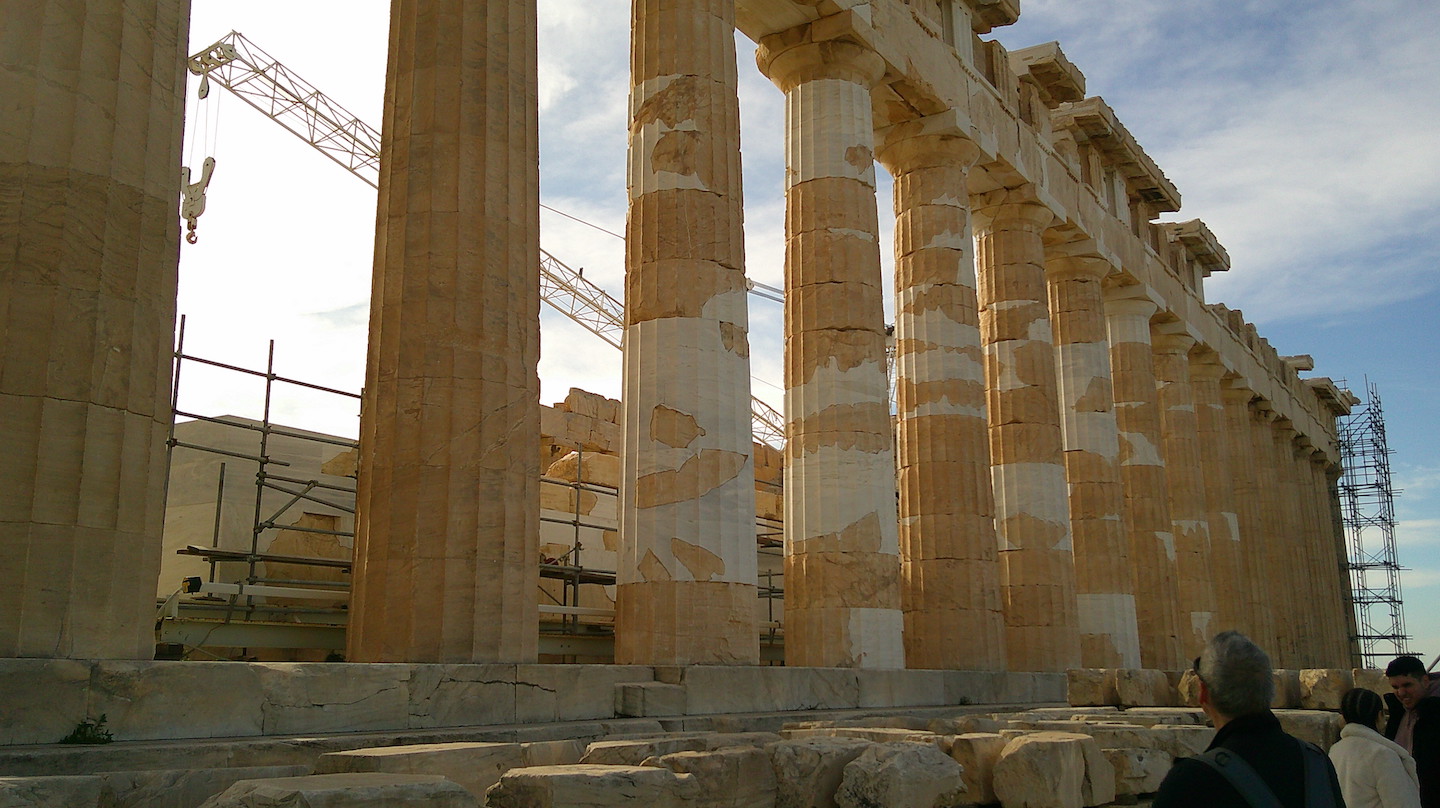 Close-up view of the Parthenon's columns on the Acropolis, showcasing the detailed Doric architecture and restoration efforts with construction equipment visible in the background.