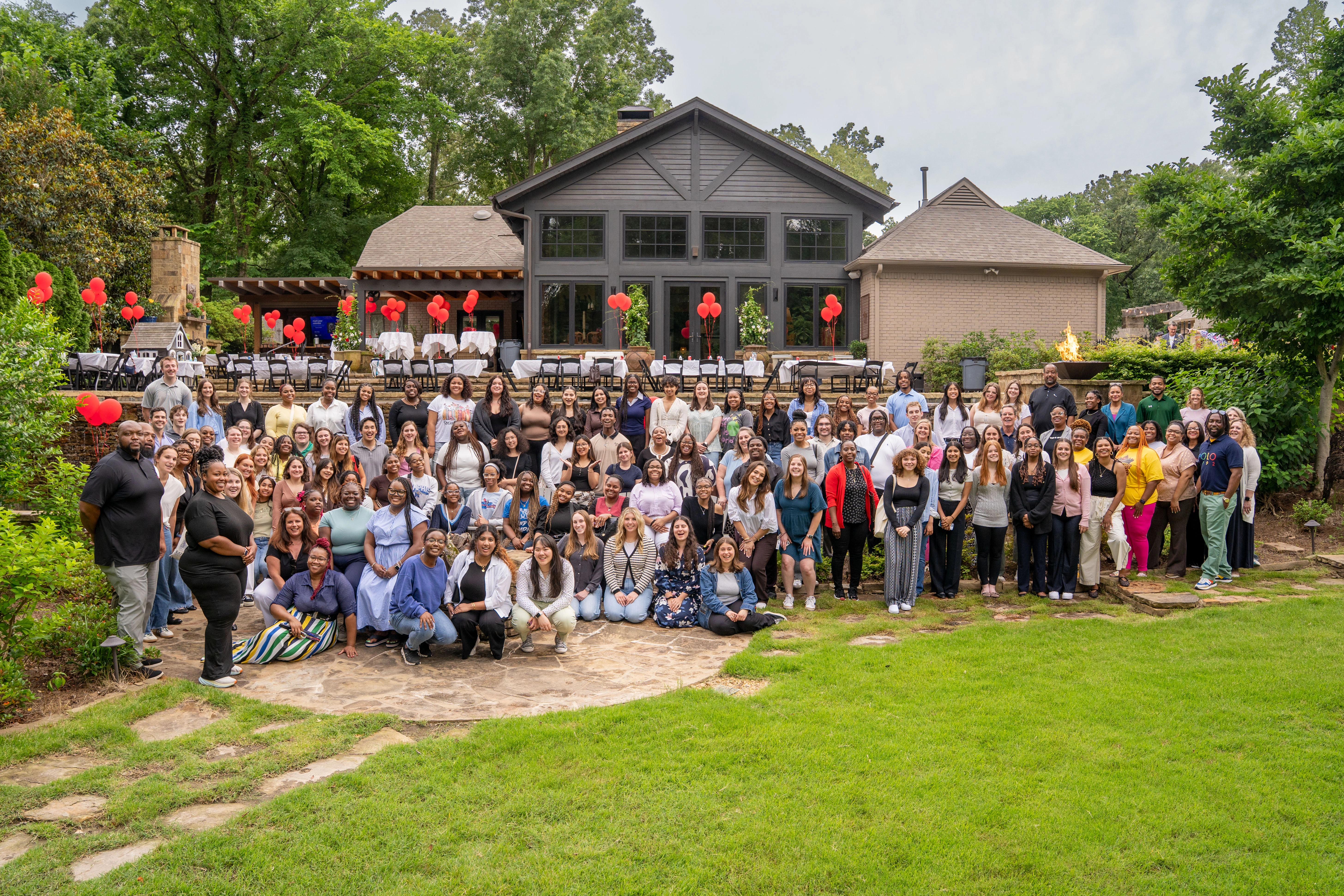  A large group of diverse individuals poses for a photo outside a building at Youth Villages, surrounded by greenery and decorative red balloons. The gathering showcases a sense of community and collaboration among staff and supporters.