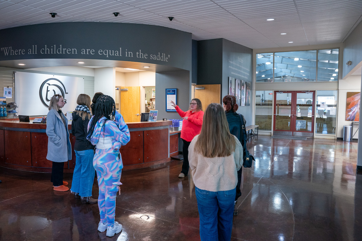 O’More students tour the Saddle-Up! campus, listening to a staff member beneath the quote, “equal in the saddle.”