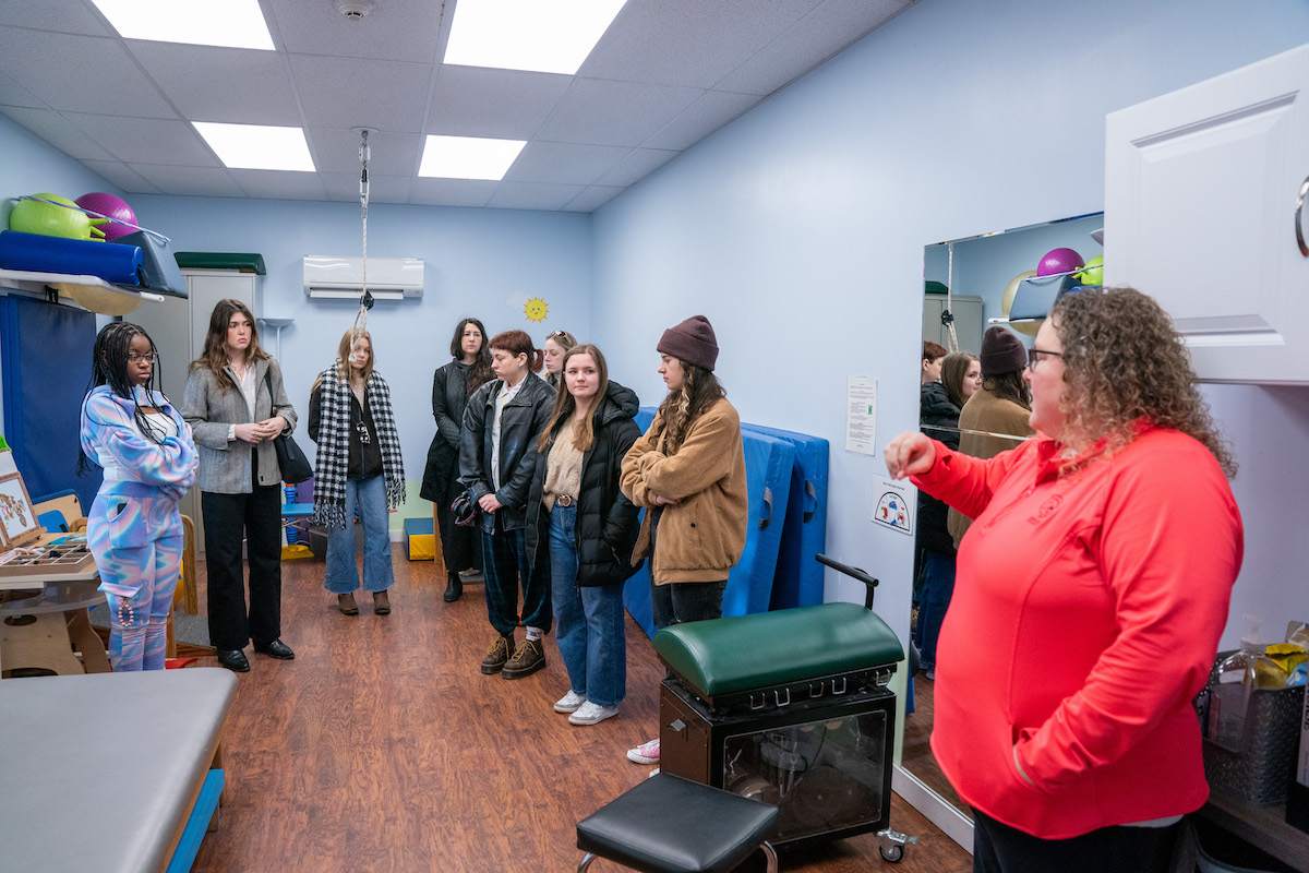 Students listen to a staff member explain therapy services in a colorful, equipment-filled room at Saddle-Up!