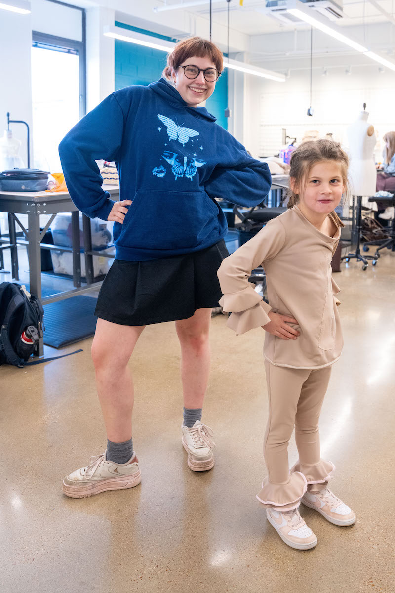 Student designer and young model strike matching poses in the studio.