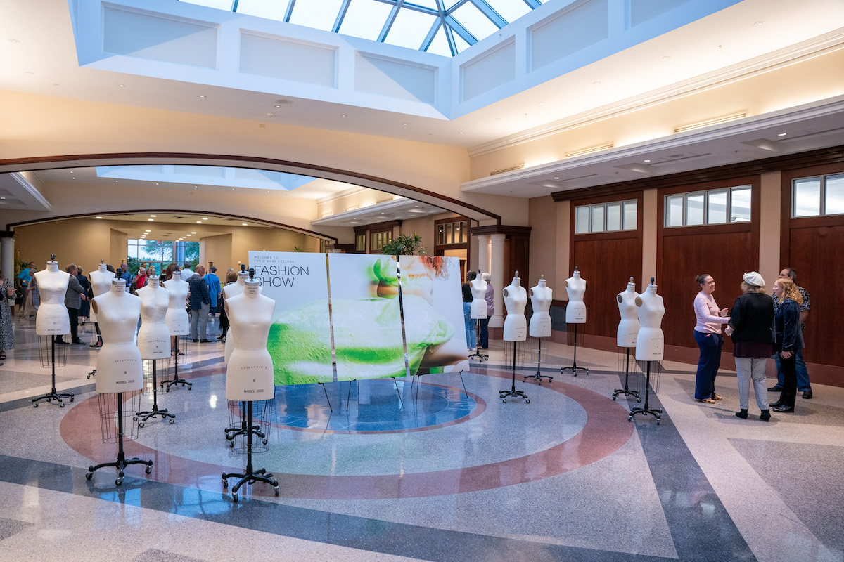 Dress forms line the atrium entrance, welcoming guests to the O’More College Fashion Show with a large branded backdrop in the center.