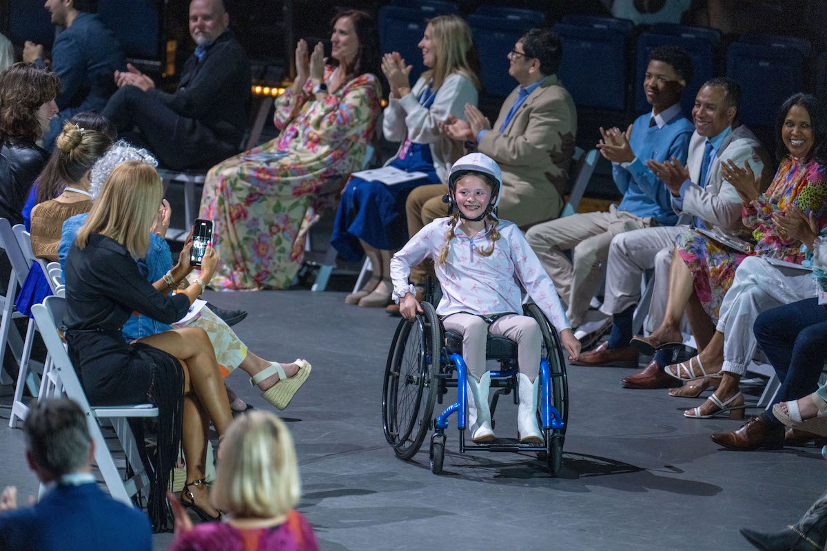 Young model in wheelchair beams as she rolls down the runway, warmly cheered on by the audience.