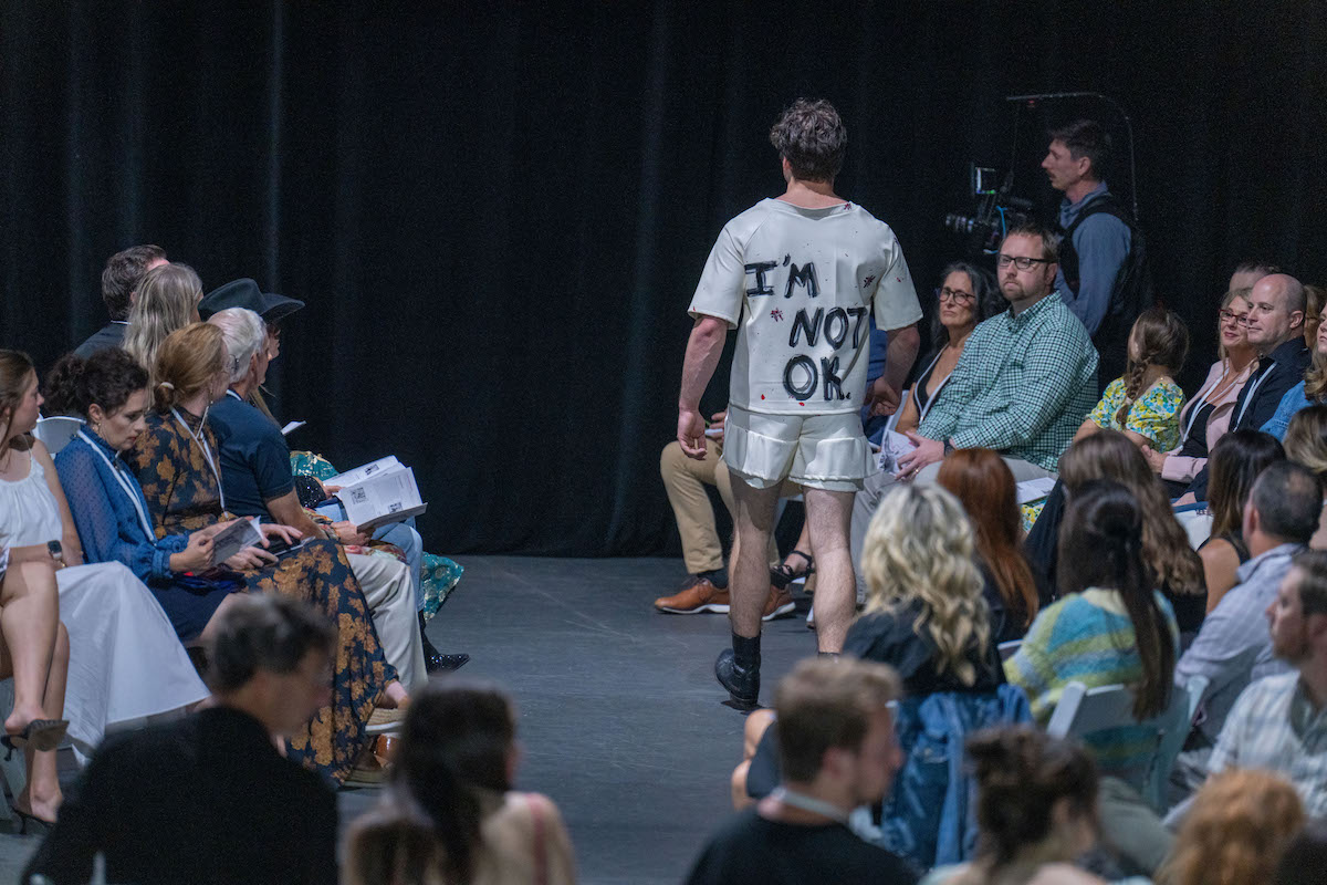 Model walks runway in statement outfit reading “I’M NOT OK."