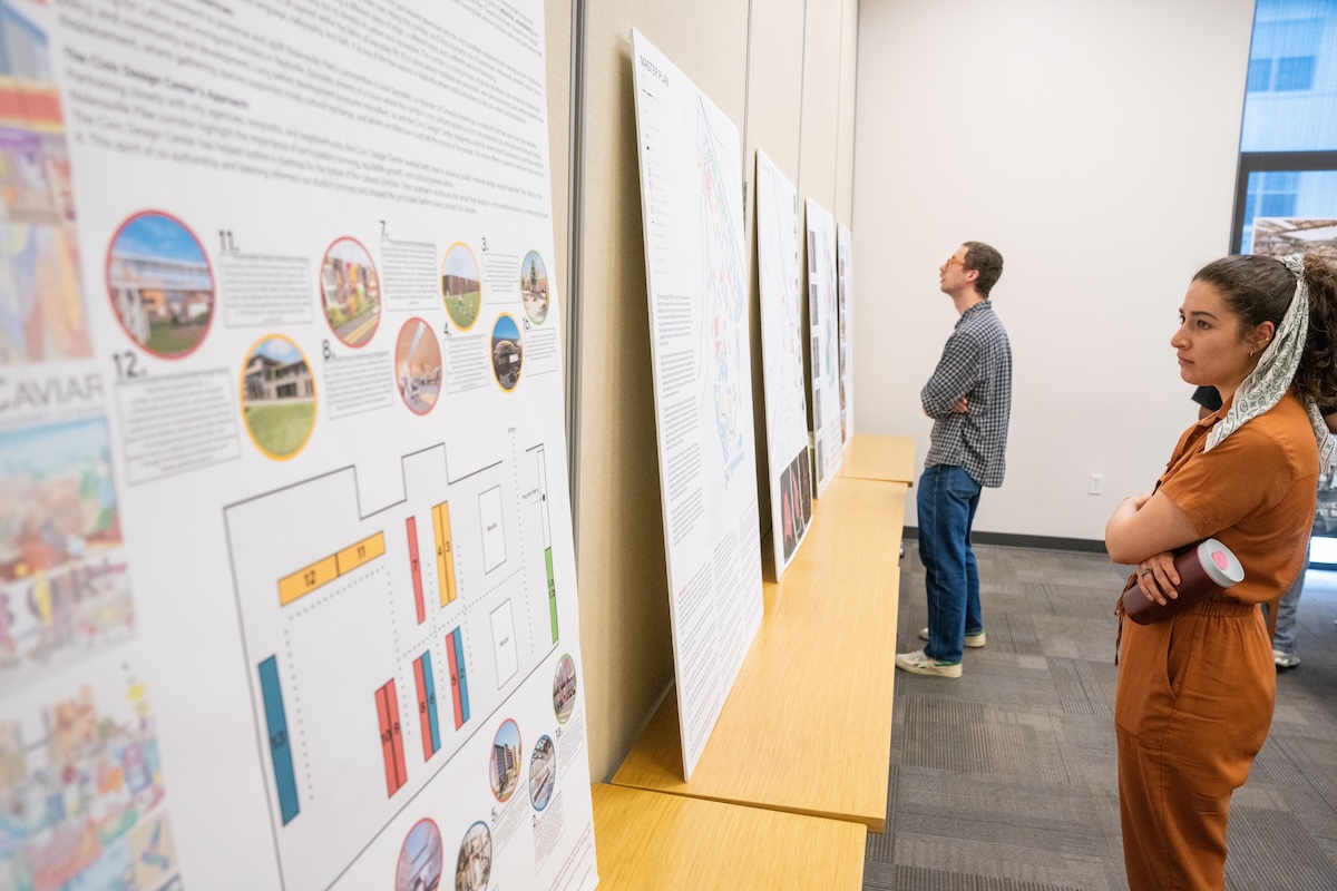 Guests examine architectural project boards lined up along the wall during the student design exhibition.