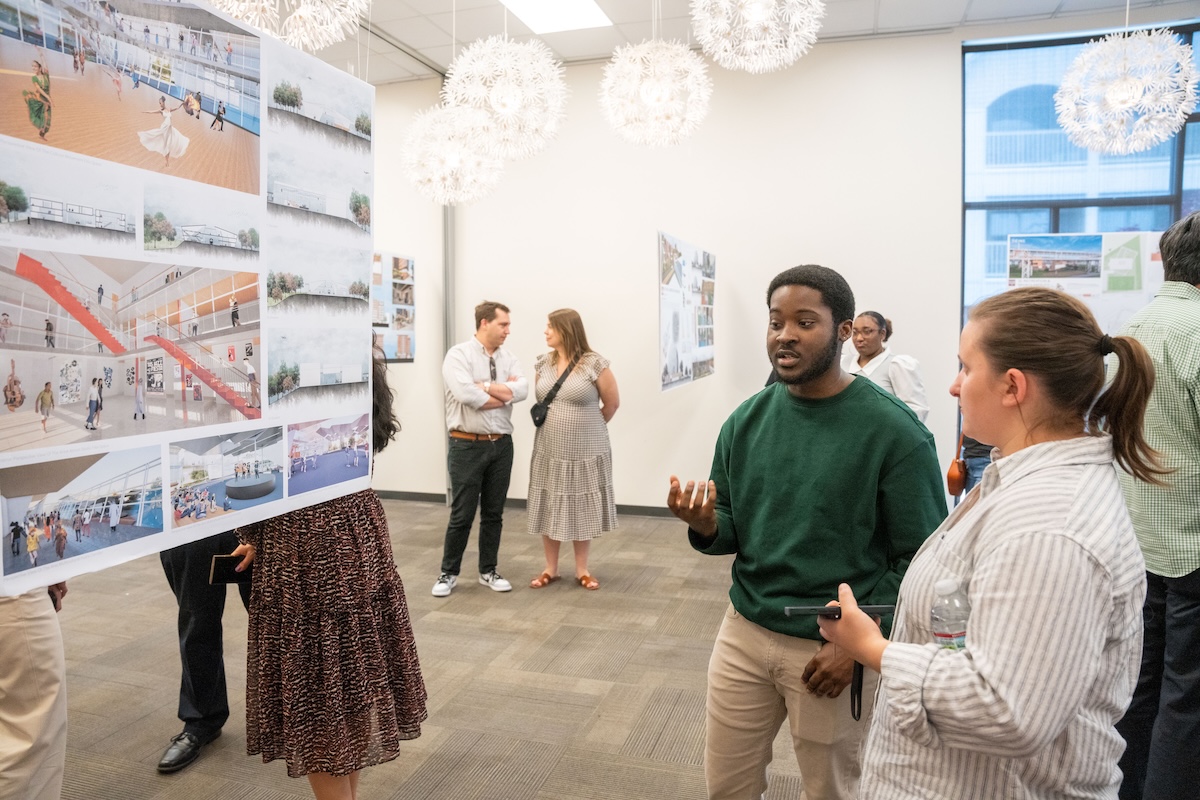 Two attendees discuss a design board featuring architectural renderings and community space concepts.
