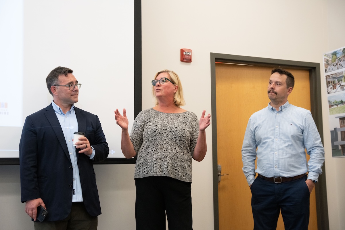 Three O'More staff/faculty stand at the front of the room during remarks at the student architecture showcase.