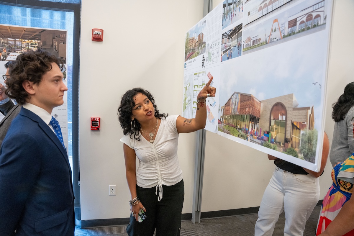 Student gestures while presenting her architectural design board to a group of guests and faculty.