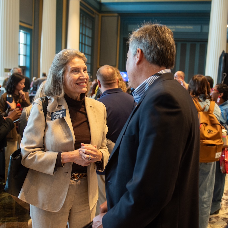 two individuals in business suits having a conversation with many others in the background