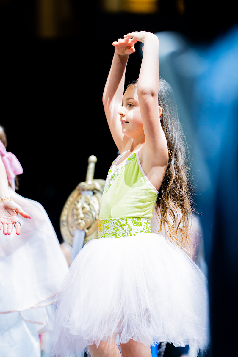 Young model in tutu poses gracefully on runway in ballet-inspired look with green and white accents.