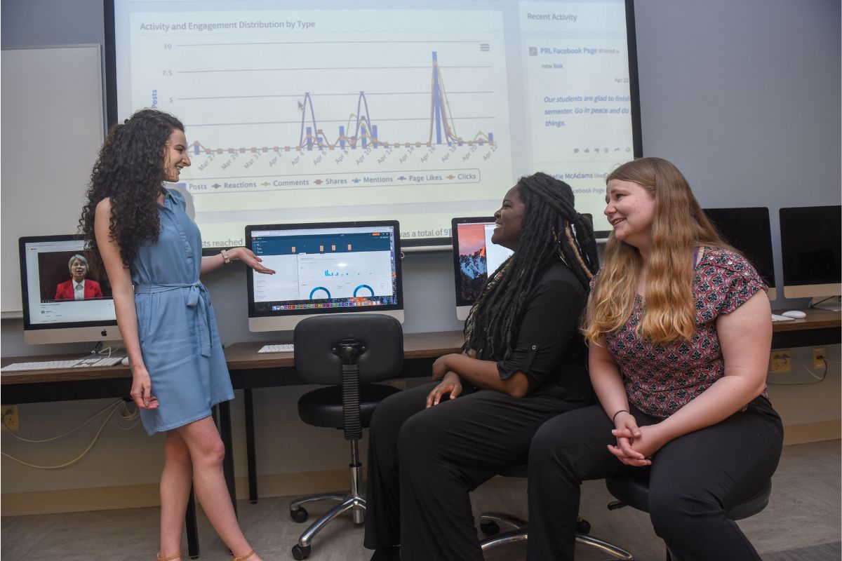 students discuss social media metrics in front of their numbers projected on a screen
