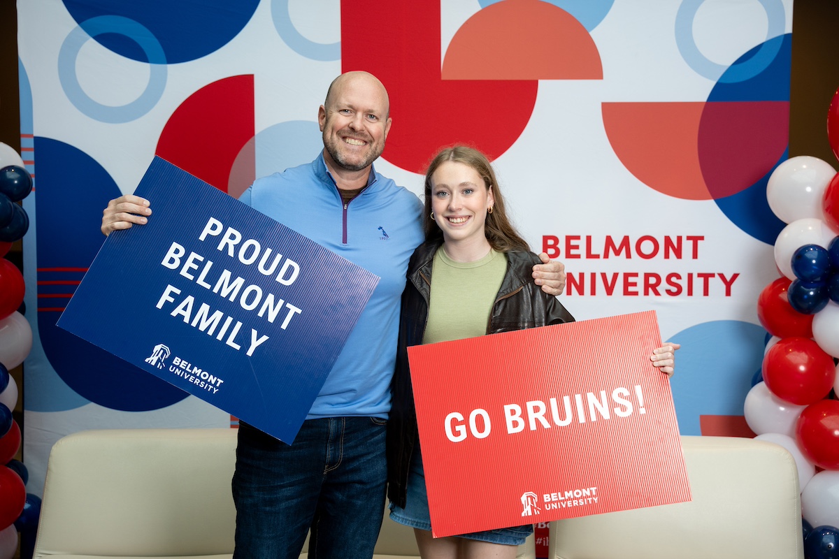 student and parent posing in front of Belmont backdrop with signs that read "proud Belmont family" and "go bruins"