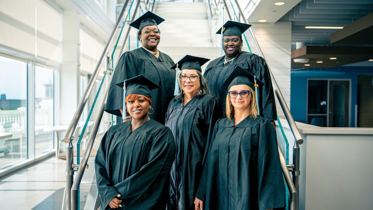 five graduates on stair in caps and gowns