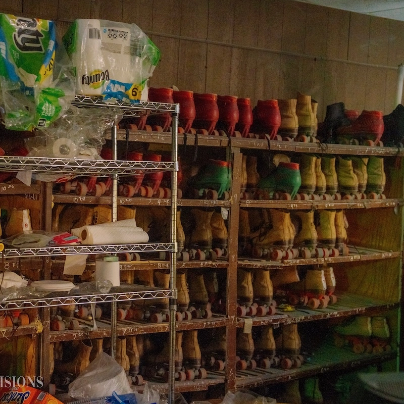 A storage area filled with shelves of colorful roller skates in various sizes, alongside supplies such as paper towels and plastic wrap. The setting appears to be part of a recreational facility, showcasing the equipment available for skating activities.