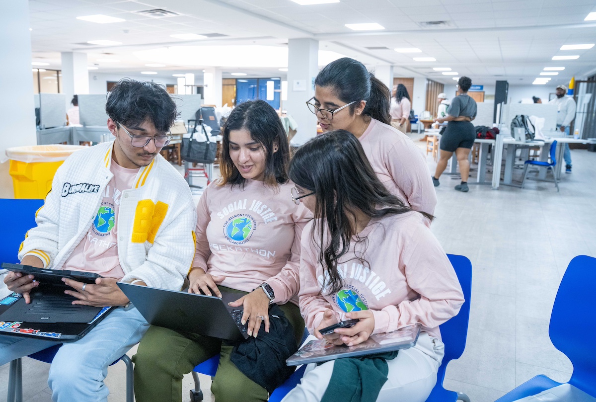students wearing "fisk-belmont hackathon" shirts looking at a computer in a large room