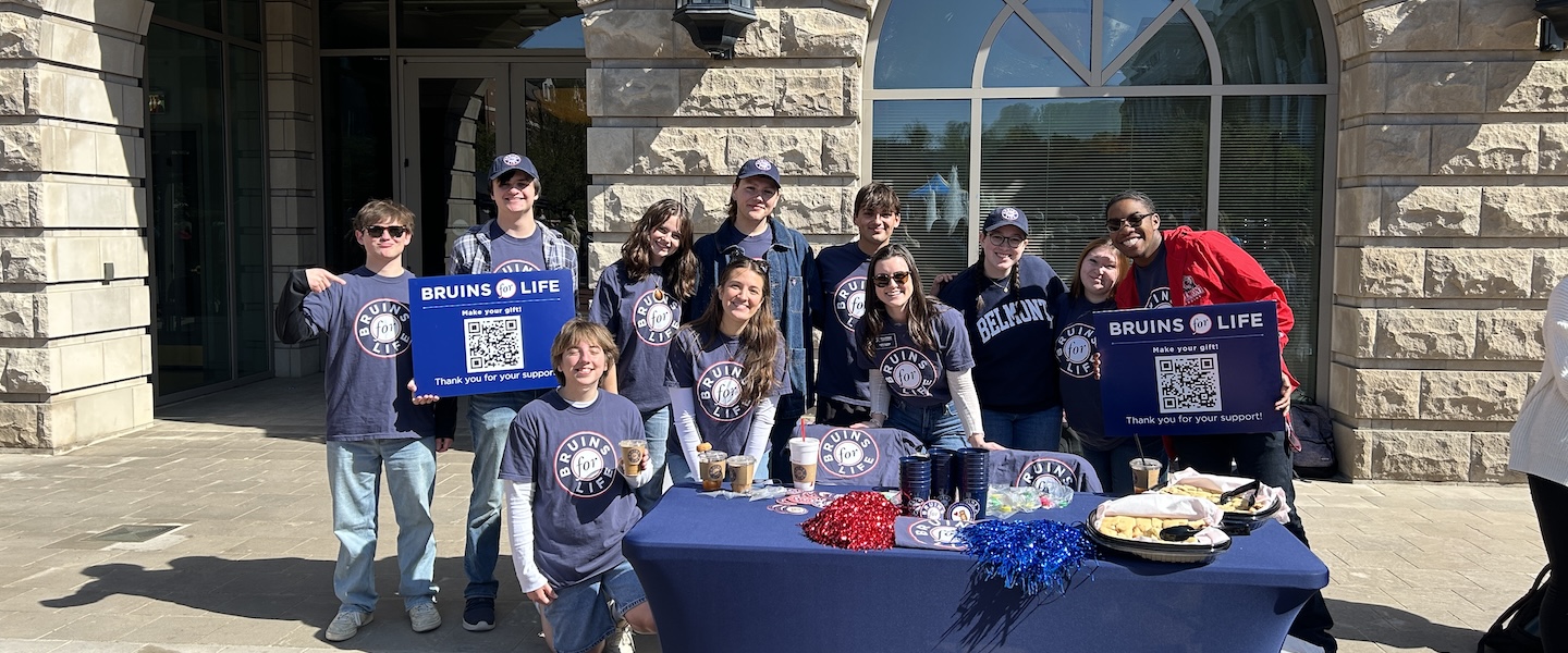 A group of Bruins for Life volunteers outside at a table holding up signs with QR codes.