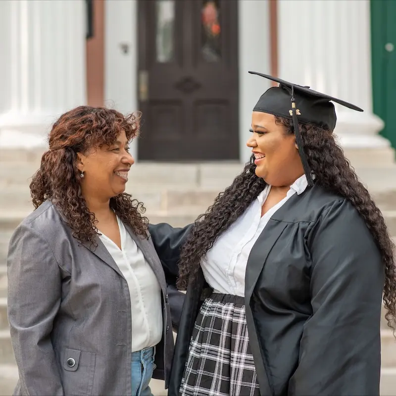 O'More alumna Janet Reyes shares a joyful moment in graduation attire with her mom outside.