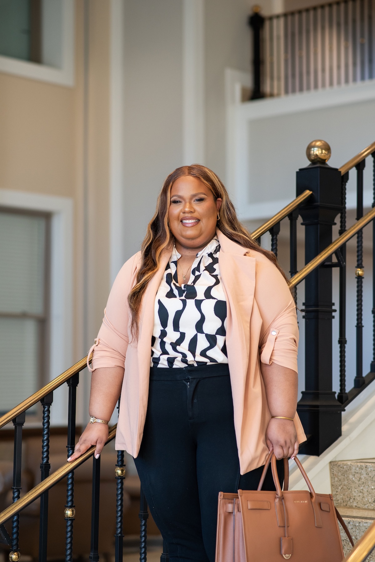 O'More alumna Janet Reyes stands confidently indoors, smiling on a staircase in business attire.