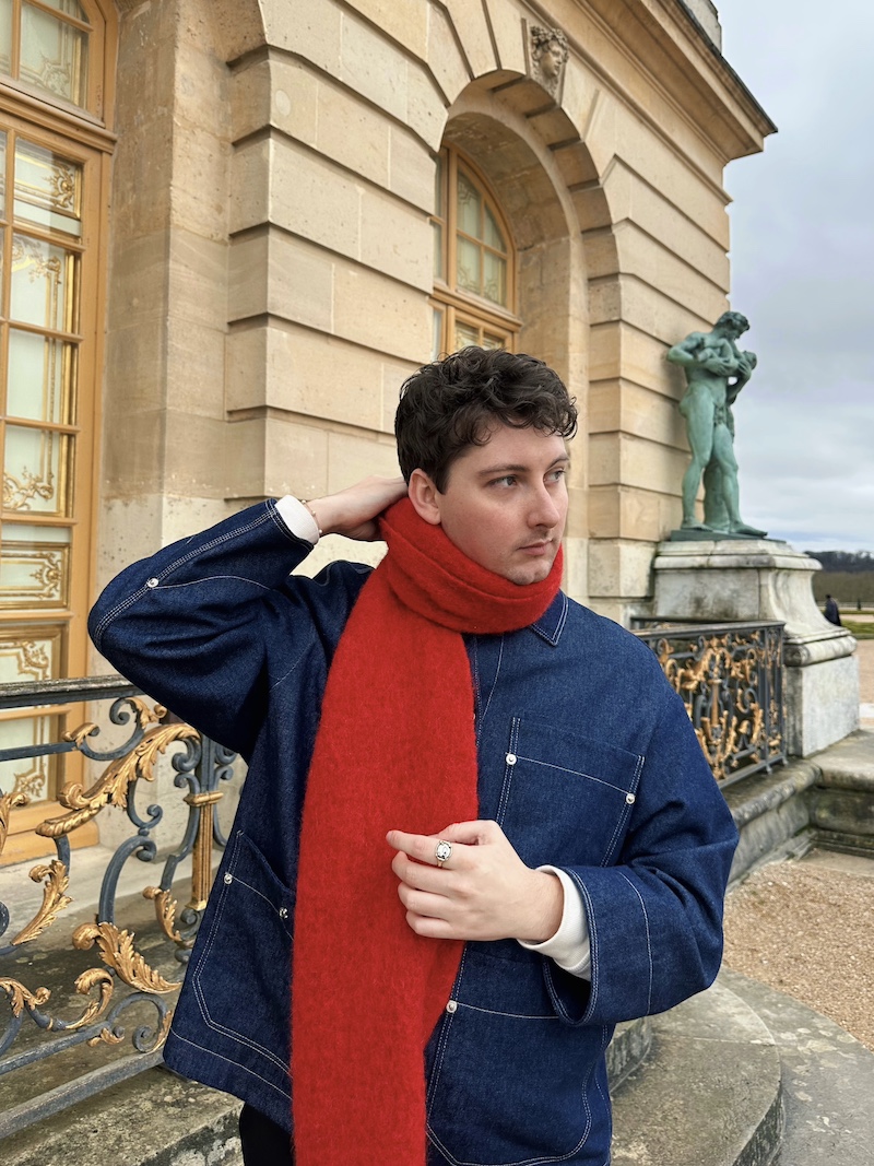 ;uke Rogers in a blue shirt and red scarf in front of an old building