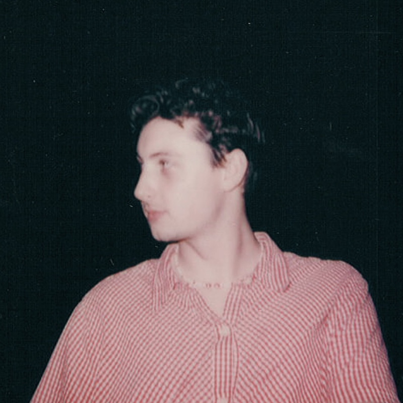 blurry polaroid-style image of Luke Rogers in a red collared shirt looking to the left