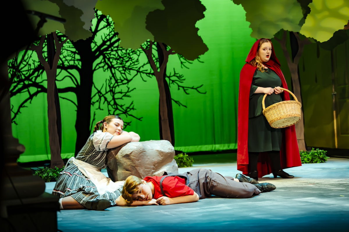 Hansel and Gretel asleep on a rock while Red Riding Hood sings on stage in "Hansel and Gretel" opera