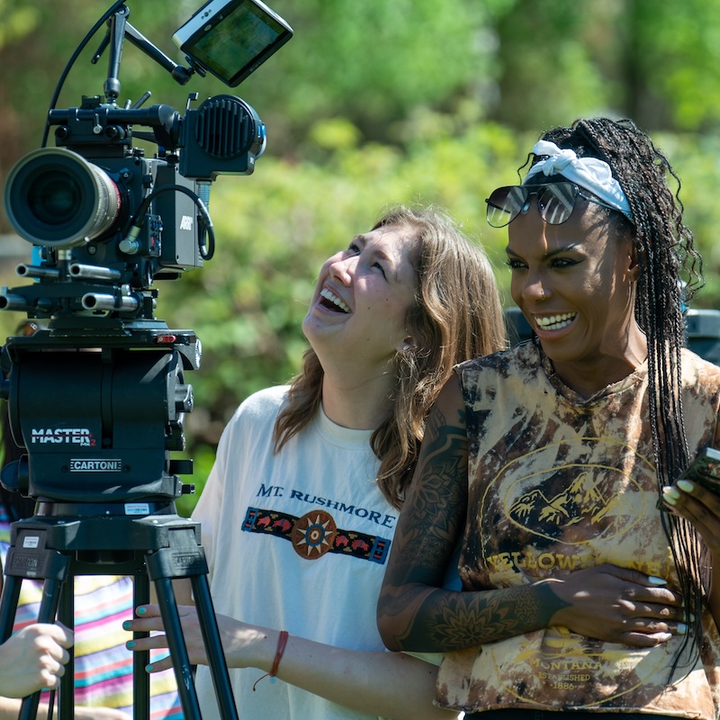 Two Belmont film students smile and laugh while working with a professional-grade camera during an outdoor film shoot.