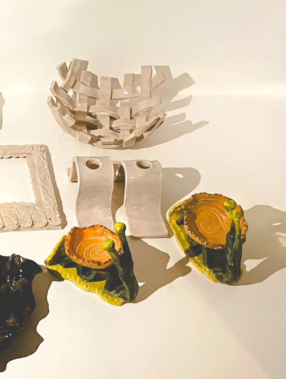 O'More students' pottery: A collection of ceramic objects displayed on a white surface, including a variety of uniquely shaped decorative pieces..