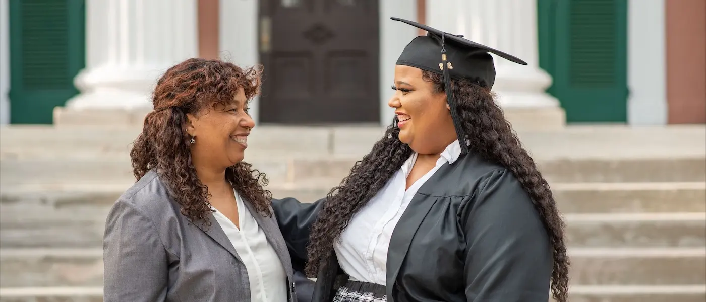 O'More alumna Janet Reyes shares a joyful moment in graduation attire with her mom outside.
