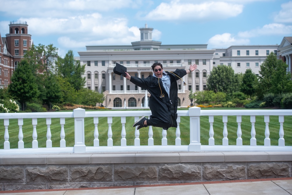 student jumps in cap and gown