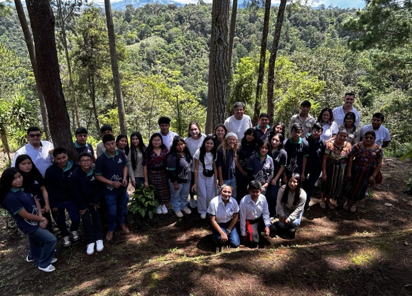 A large group of students and community members stand together on a wooded hillside.