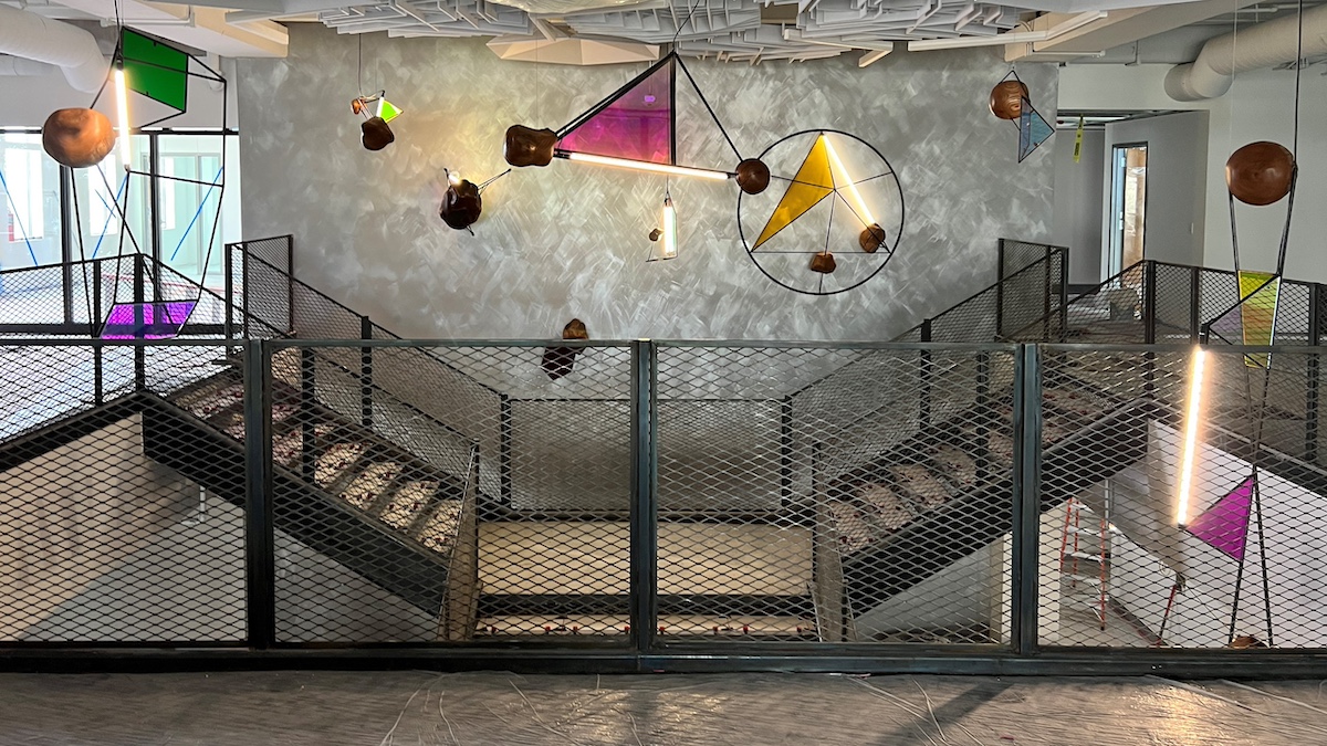 wide stairwell with panels of stained glass and metal rods in a curated design hanging overhead