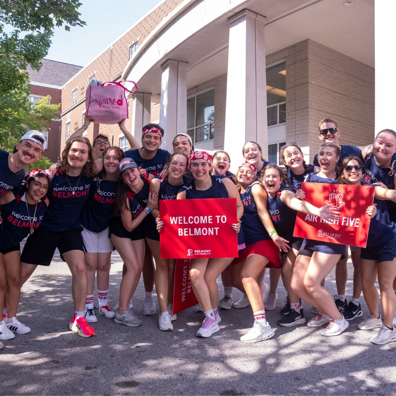 Smiling Belmont University students and orientation leaders welcome new students to campus with 'Welcome to Belmont' signs.