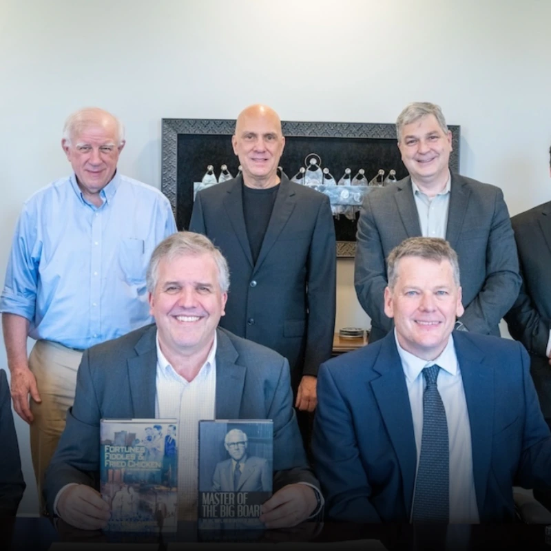 Professional men and women seated at a boardroom table with books and cassette tapes