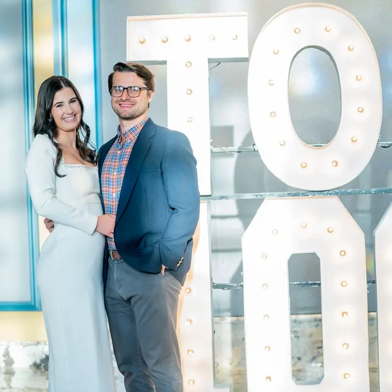 Alumna and spouse posing in front of Top 100 sign
