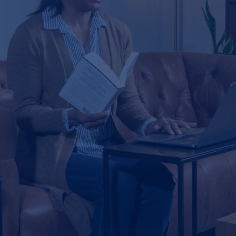 a woman sitting at a computer holding a book