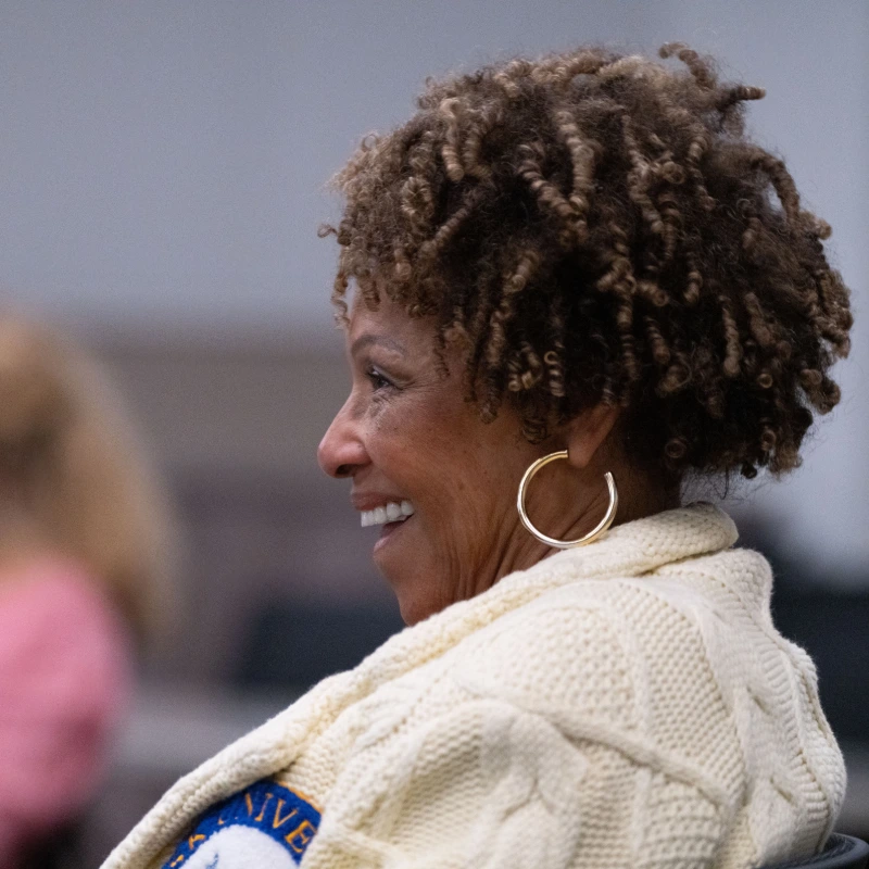 Happy woman with curly hair and gold hoop earrings smiling, wearing a cream cable-knit sweater.