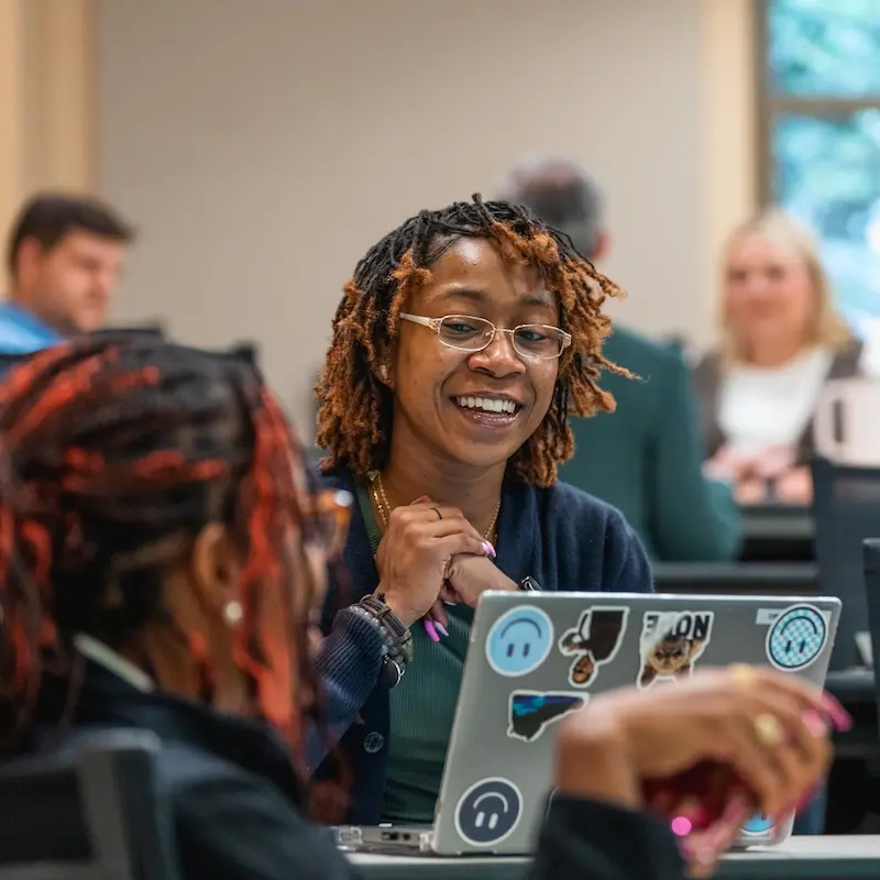 Student smiling and talking with laptop open in front of her