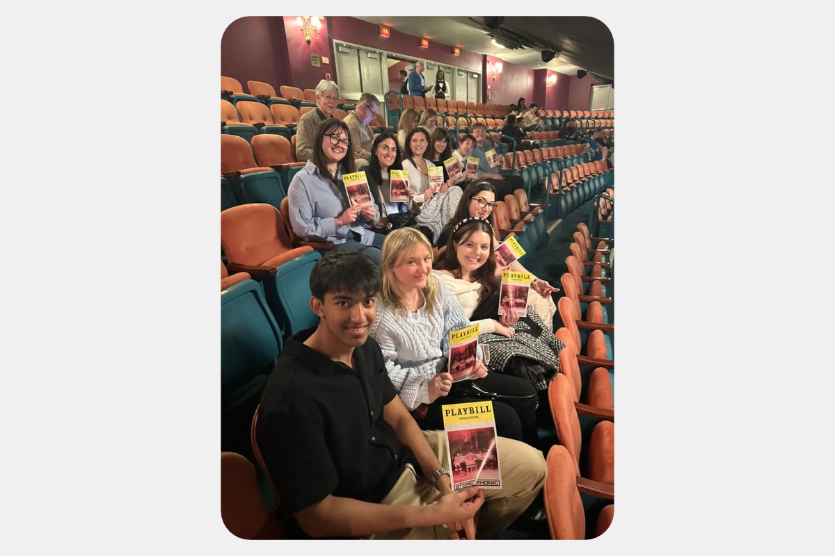 Group of smiling students holding Playbills in a theater audience, ready for a performance.