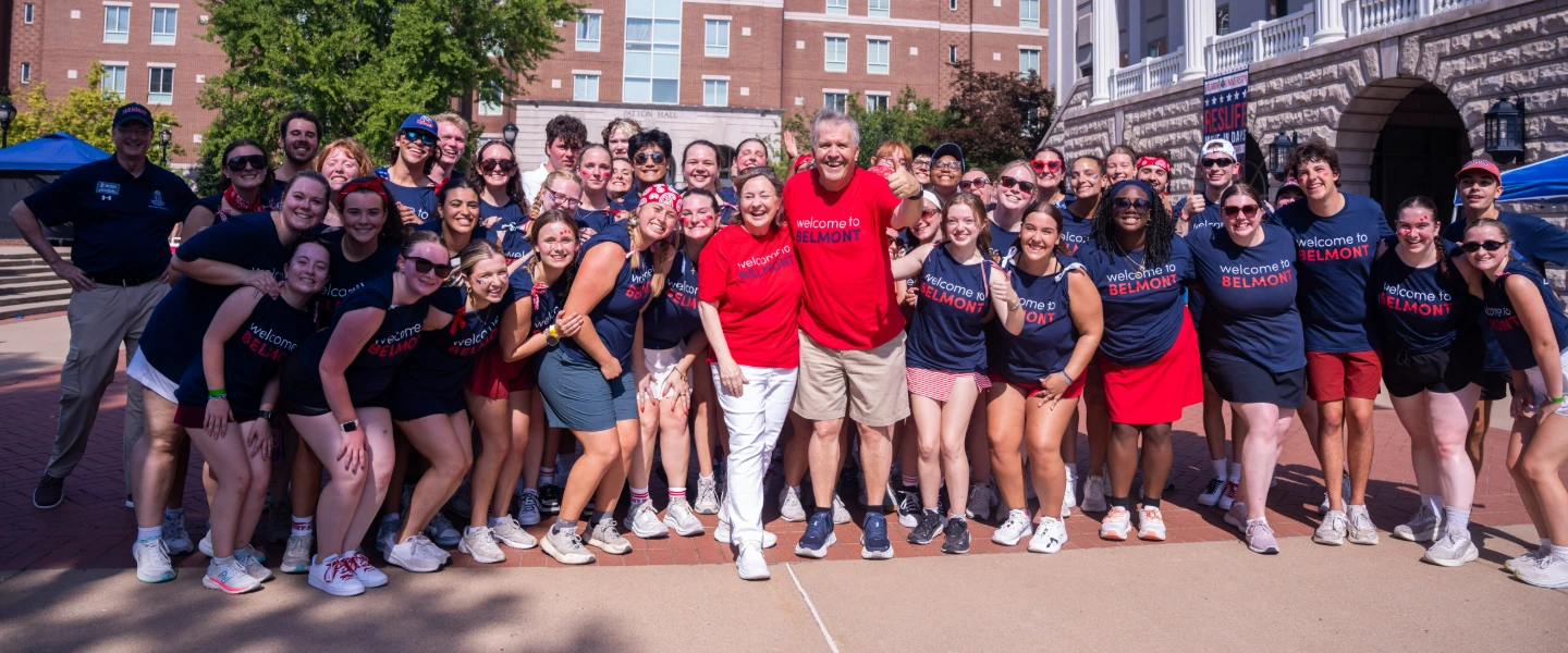 Greg and Susan Jones stand with group of Belmont students and staff in "Welcome to Belmont" shirts on campus during orientation.