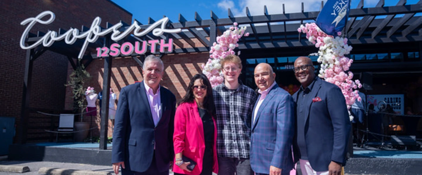 Five people in front of Coopers 12 SOUTH restaurant with pink cherry blossom decor in Nashville.