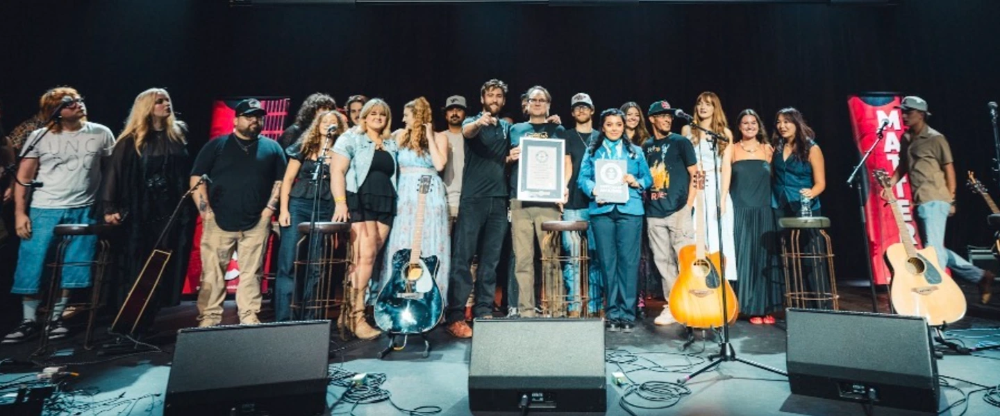 Group of artists on stage celebrating a Guinness World Records official attempt, holding awards near guitars.